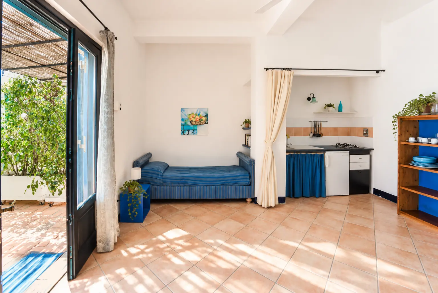Il soggiorno luminoso con letto singolo blu e porta sul giardino
